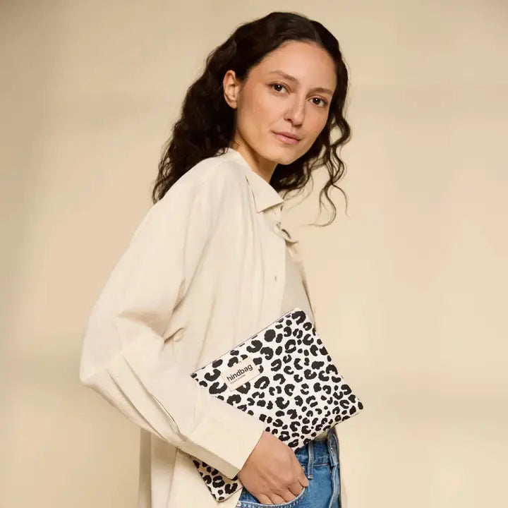 A woman wearing a cream button-up shirt and blue jeans holds a black and white leopard print clutch bag with a visible 'Society6' brand label.